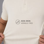 Close-up of a person wearing a light cream polo shirt with a black printed graphic that reads 'NON-IRON WRINKLE-FREE' with a no-iron symbol.